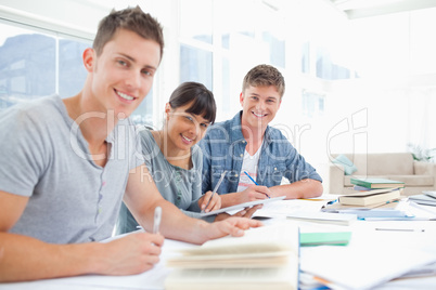 Three smiling students doing homework as they look into the came