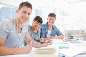 Three smiling students doing homework as they look into the came