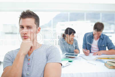 A thinking student looking into the camera with his friends behi