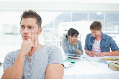 One student standing and thinking as his friends work behind him