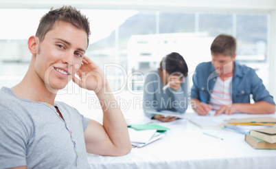 A smirking student sits in front of his friends as he looks into