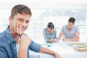 A smiling male sitting in front of his friends as he looks at th