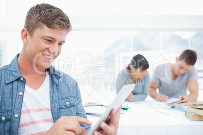 A smiling male using his tablet pc in front of his friends