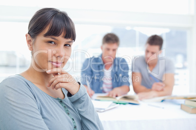 A woman looking at the camera thinking with her friends studying