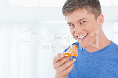 A man with a piece of pizza as he looks at the camera