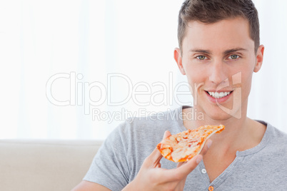 A man sitting as he holds a slice of pizza