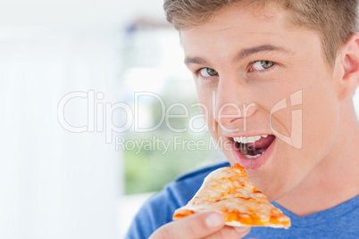 A man with a slice of pizza in his hand as he looks at the camer