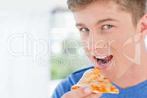 A man with a slice of pizza in his hand as he looks at the camer