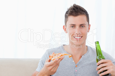 A man smiling with beer in one hand and pizza in the other