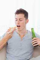 A man with a piece of pizza and some beer in his hands