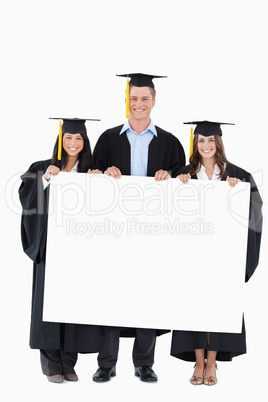 Full length of three graduates from college holding some blank p