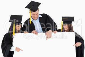 Three graduates pointing to the blank sign