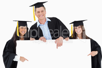 Three graduates pointing to the blank sign as they look at the c