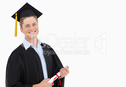 A smiling man with a degree in hand as he looks at the camera