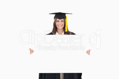 A woman in her graduation gown holds a blank sheet in front of h