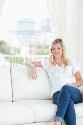 A woman with her arm resting on the couch as she sits and smiles
