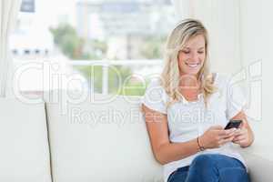 A woman sitting on the couch smiling as she uses her phone