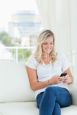 A woman smiles while using her phone on the couch