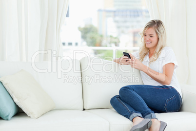 A woman sitting on the couch to the side as she uses her phone