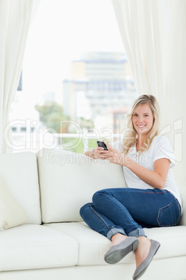 A woman sitting sideways on the couch as she uses her phone and