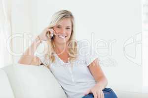 Side view of a woman on her couch smiling as she talks on the ph