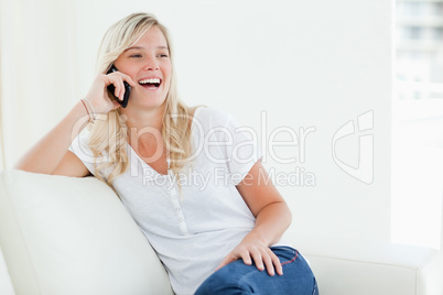 A laughing woman on her phone as she sits on the couch