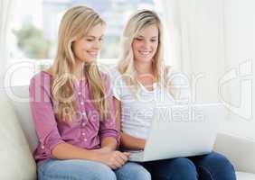 A girl and her friend looking into a laptop while on the couch