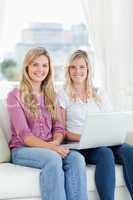 Two sisters sit together and smile with a laptop while looking a