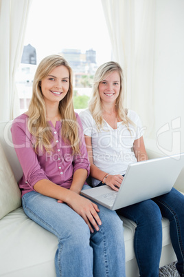 Two sisters sit together on the couch as they look at the camera