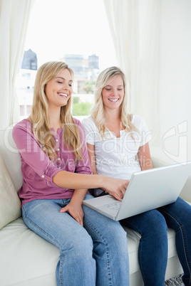 Two smiling sisters watch a tv show on the laptop