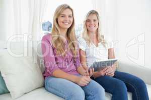 Two sisters looking at the camera as they hold a tablet pc in th