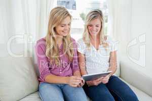 Two sisters sit on the couch as they look at a tablet