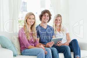 Three young adults look at the camera as they hold a tablet in t