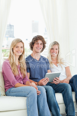 Two sisters and a brother sit on the couch looking at the camera