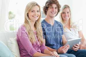 Three smiling people sit together on the couch with a tablet