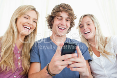 Three friends looking at the screen of a mobile phone while smil