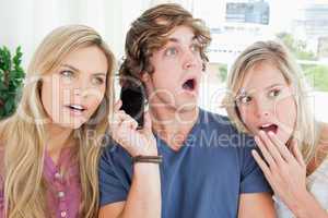 Three shocked friends listening to a phone conversation