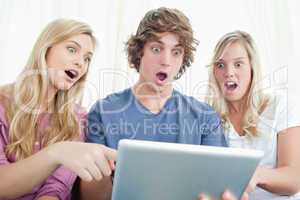 Three shocked friends looking at the screen of the tablet