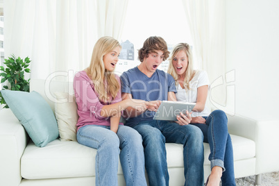 Three friends looking at the screen of the tablet in shock and p