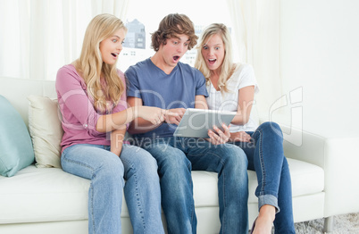 Three friends looking at the screen of the tablet in shock and p
