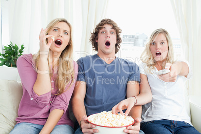 Three friends enjoying popcorn together while shocked at the tv