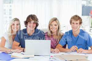 A group of students with a laptop look into the camera