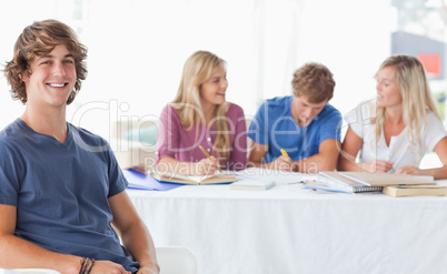 Smiling man sitting on front of his friends and looking at the c