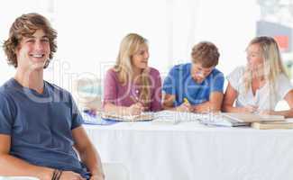 Smiling man sitting on front of his friends and looking at the c
