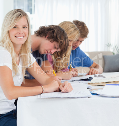 A smiling girl looks at the camera as her friends study