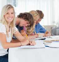 A smiling girl looks at the camera as her friends study