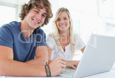 A smiling couple with a laptop looking at the camera