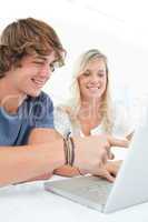 A smiling couple look at the laptop as the man points to the scr