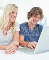 A smiling couple sit together as they surf the internet