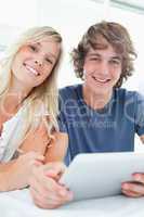 A smiling couple holding a tablet and looking at the camera